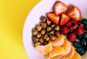 Close-up of a bowl with fresh fruits and nuts against a vibrant yellow backdrop.