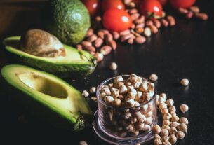 Fresh avocado, chickpeas, nuts, and tomatoes on a dark table, perfect for healthy recipes.