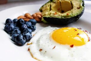 A nutritious breakfast featuring a fried egg, avocado, blueberries, and almonds.