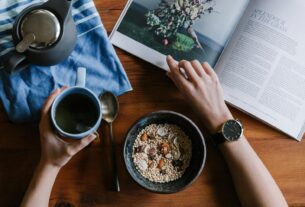 Top view of a healthy breakfast setting with muesli, tea, and magazine on wooden table.