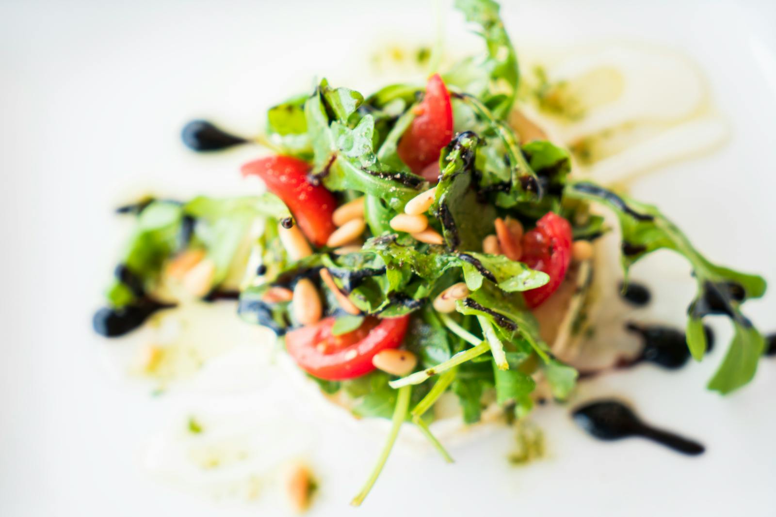 A vibrant arugula salad with cherry tomatoes, pine nuts, and balsamic glaze.