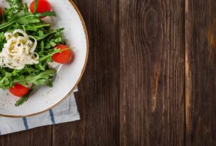 A delightful arugula salad with tomatoes and cheese, served on a rustic wooden table, perfect for healthy eating.