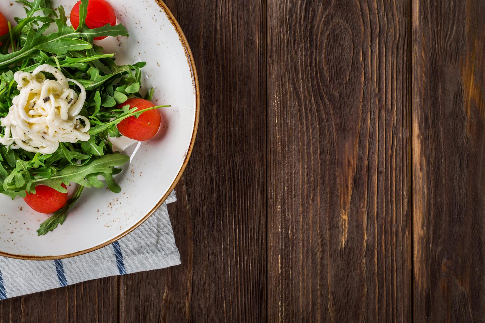 A delightful arugula salad with tomatoes and cheese, served on a rustic wooden table, perfect for healthy eating.