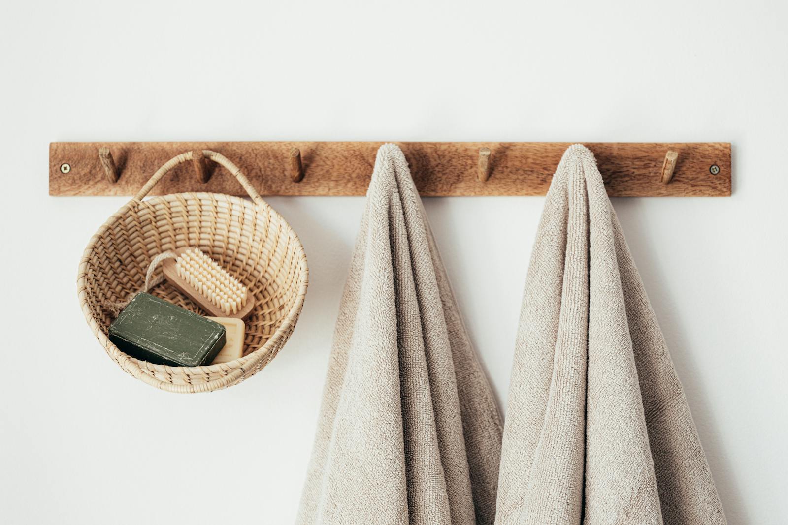 Minimalist bathroom setup featuring eco-friendly wooden hooks, towels, and basket with soap for a sustainable lifestyle.