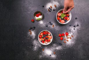 Fresh strawberries, blueberries, almonds in bowls on black table with hand arranging.