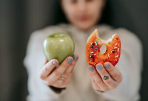 A close-up of a person holding an apple and a donut, symbolizing the choice between healthy eating and indulgence.