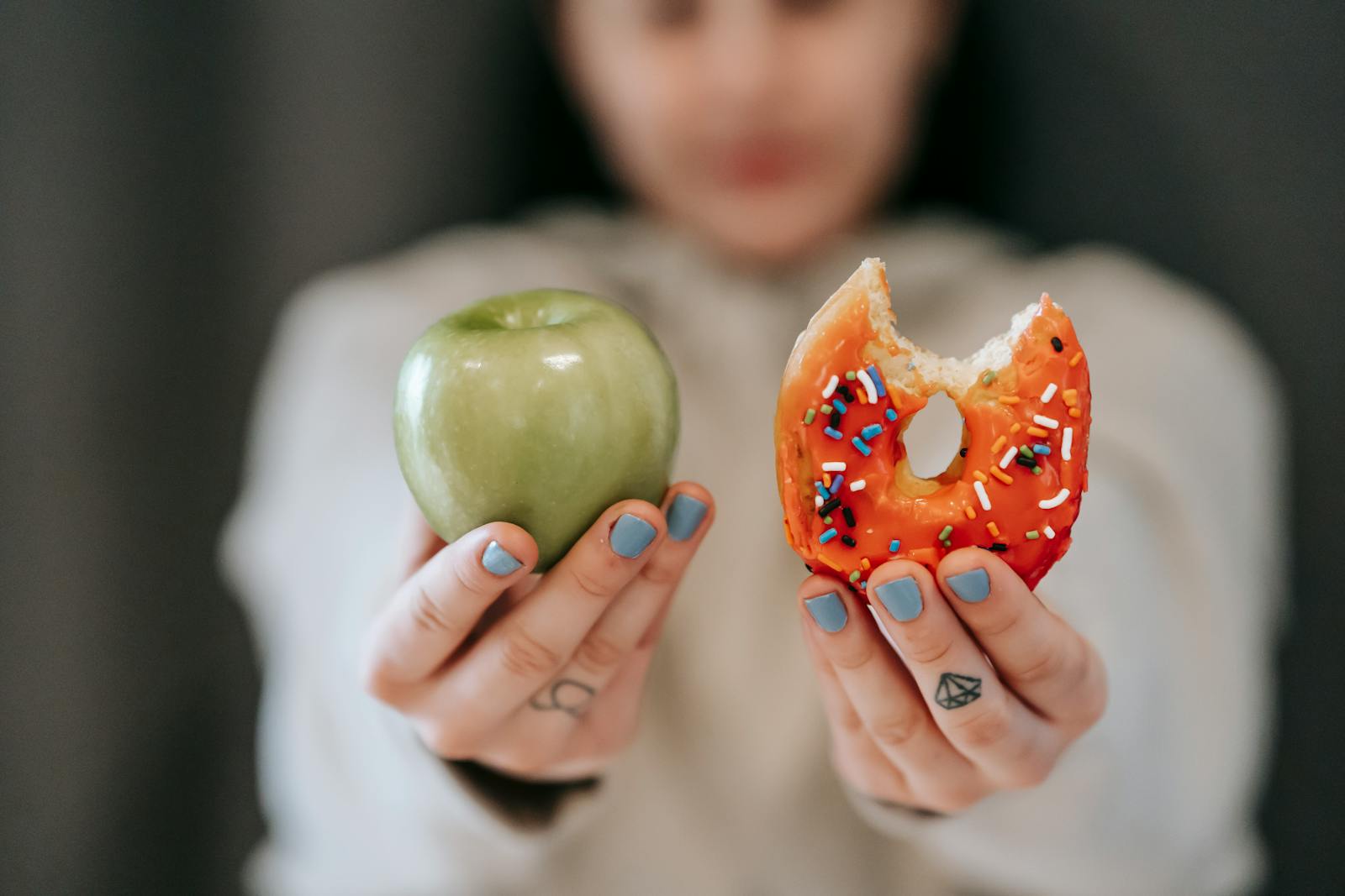 A close-up of a person holding an apple and a donut, symbolizing the choice between healthy eating and indulgence.