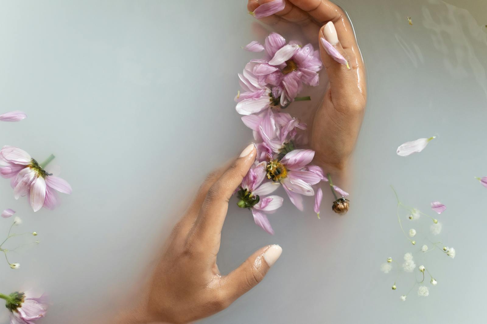 Gentle hands with pink flowers in a soothing bath, representing tranquility and skin care.