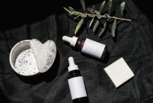 Flat lay of skincare products with gua sha and leaves on black textile. Ideal for beauty and wellness visuals.