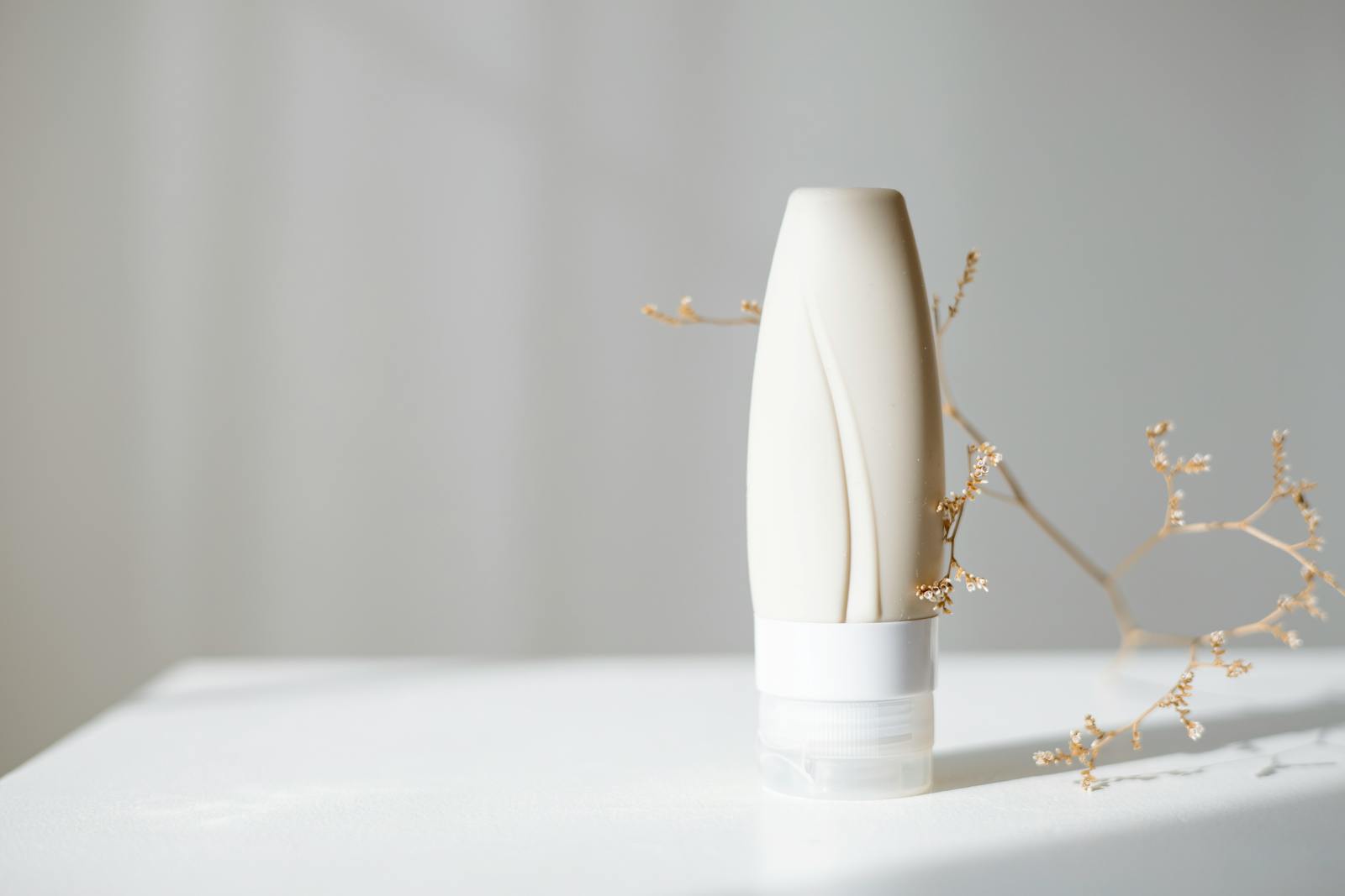 Elegant minimalist skincare bottle with dried branch, ideal for beauty and spa themes.