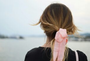 focus photography of woman with pink hair bow facing on body of water