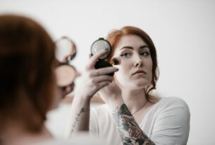 selective focus photography of woman applying blush-on on her face